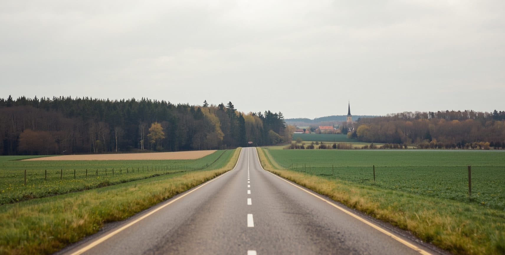 Landstraße zwischen Feldern, ein Kirchturm am Horizont